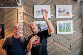 Two men standing in front of a wall with pictures on it.